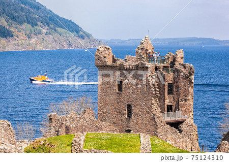 Ruins of Urquhart Castle against boat on Loch Ness in Scotland 75124310