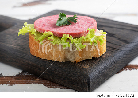 Sandwiches with lettuce leaves and sliced salami sausage on a wooden Board. 75124972