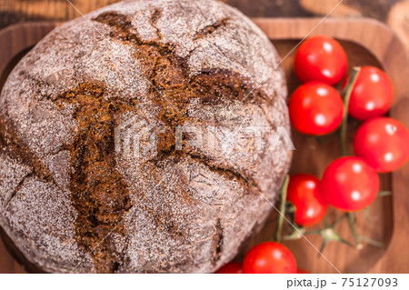 Fresh dark round bread on wooden plate close - up Fresh dark round bread on wooden plate close - up 75127093