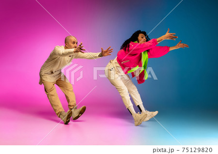 Stylish sportive caucasian couple dancing hip-hop on colorful gradient background at dance hall in neon light. 75129820