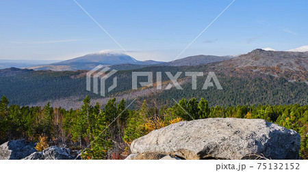 Autumn mountain landscape .Hill slope with coniferous thickets against the background of mountain ranges and blue sky. 75132152