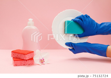 Women's hands in rubber gloves with a sponge and a plate on the pink background. Women's hands in rubber gloves with a sponge and a plate on the pink background. 75132724