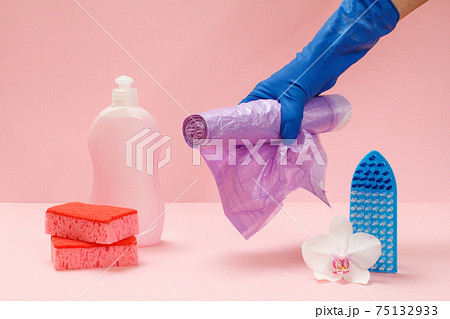 Bottle of dishwashing liquid, sponges and hand with garbage bags on pink background. 75132933
