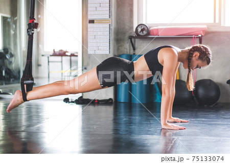 Athlete sporty woman doing exercise with fitness trx straps to strengthen his abdominal muscle in gym Athlete sporty woman doing exercise with fitness trx straps to strengthen his abdominal muscle in gym 75133074