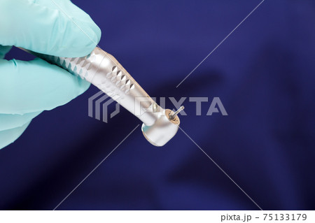 Dentist's hand in green examination glove with dental handpiece. 75133179