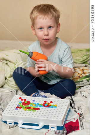 A child plays a toy screwdriver sitting 75133598