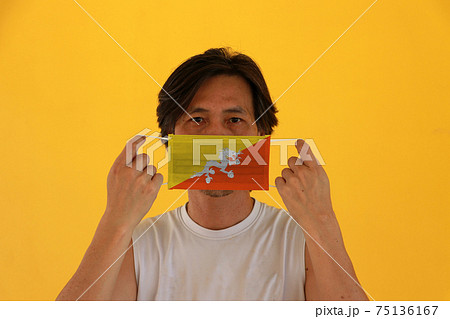A man with Bhutan flag on hygienic mask in his hand and lifted up the front face A man with Bhutan flag on hygienic mask in his hand and lifted up the front face 75136167