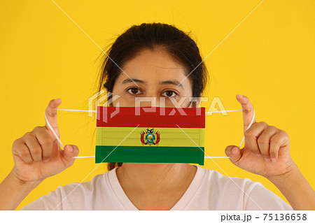 A woman in white shirt with Bolivia flag on hygienic mask in her hand and lifted up the front face A woman in white shirt with Bolivia flag on hygienic mask in her hand and lifted up the front face 75136658