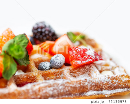 Fried waffle sprinkled with powdered sugar with pieces fresh fruits and berries 75136973