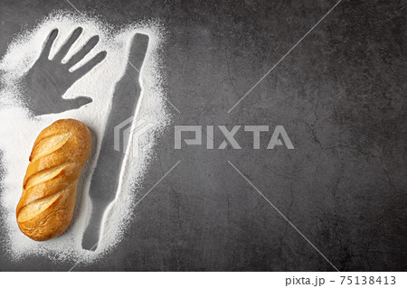 Baking dark background with fresh whole loaf of bread and outlines of ingredient flour of rolling pin and imprint of human hand top view with copy space Baking dark background with fresh whole loaf of bread and outlines of ingredient flour of rolling pin and imprint of human hand top view with copy space 75138413