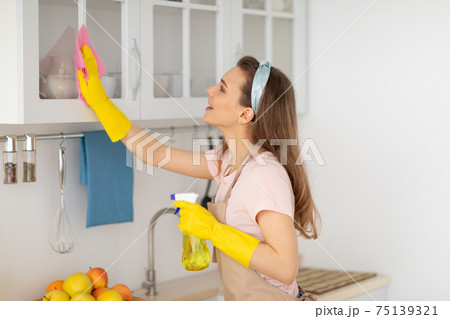 Lovely millennial housemaid wiping kitchen cabinet, performing house cleanup 75139321