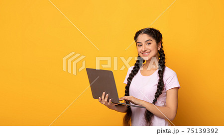 Confident young indian woman holding and using laptop 75139392