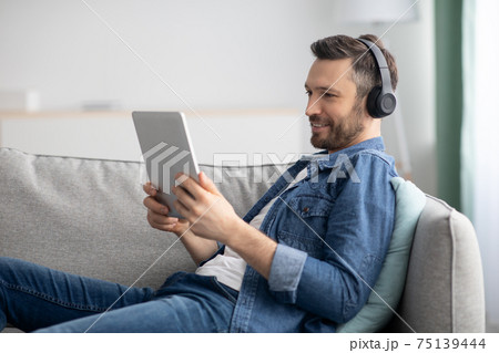 Joyful middle-aged man usind headset and digital tablet Joyful middle-aged man usind headset and digital tablet 75139444