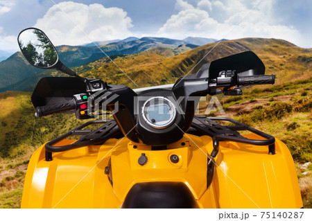 Yellow offroad touring atv vehicle standing on a mountain offroad trail steering wheel view. Yellow offroad touring atv vehicle standing on a mountain offroad trail steering wheel view. 75140287