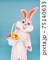 Easter bunny or rabbit or hare with basket of colored eggs, shows index finger, having fun, celebrates Happy easter. Easter rabbit isolated on blue background 75140633