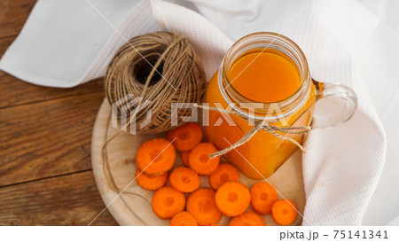 Bright orange carrot juice and a skein of twine on a wooden background 75141341