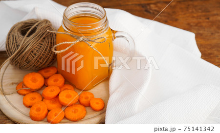 Bright orange carrot juice and a skein of twine on a wooden background Bright orange carrot juice and a skein of twine on a wooden background 75141342