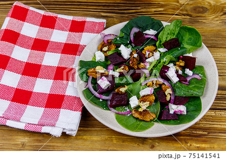 Tasty spinach salad with boiled beetroot, feta cheese, walnut and red onion on wooden table. Healthy vegetarian food 75141541