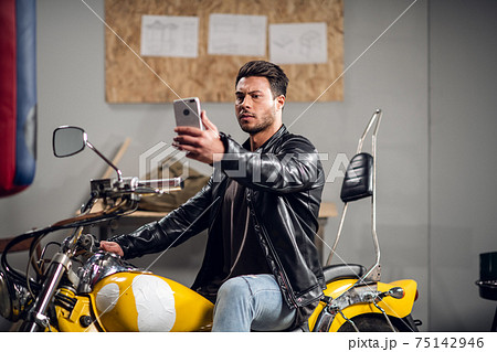 A stylish guy on a yellow cool motorcycle takes a selfie in a garage or car repair shop 75142946