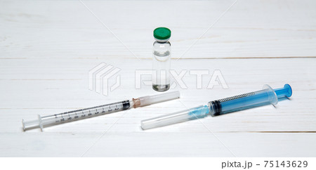 two syringes for injections and bottle with a vaccine lie on light wooden table two syringes for injections and bottle with a vaccine lie on light wooden table 75143629