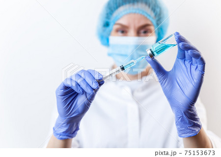 Doctor in gloves filling up syringe from bottle with vaccine, medicine Doctor in gloves filling up syringe from bottle with vaccine, medicine 75153673