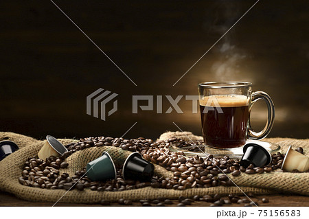 Cup glass of coffee with smoke, coffee beans and coffee capsules on burlap sack on wooden background Cup glass of coffee with smoke, coffee beans and coffee capsules on burlap sack on wooden background 75156583