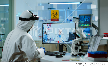 Chemist in ppe suit listening professional doctor on video call Chemist in ppe suit listening professional doctor on video call 75156675