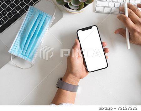 Businessman holding smartphone with mock up screen in his hand while typing on computer keyboard Businessman holding smartphone with mock up screen in his hand while typing on computer keyboard 75157525