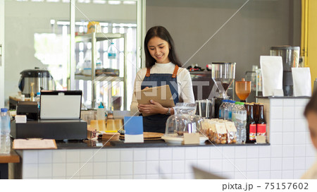 Female barista with apron writing an order while standing at counter bar in coffee shop 75157602