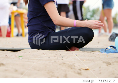 Yoga on the beach. Close-up of girls legs in lotus position. Blurred background for signature. Doing sports, Pilates, stretching outdoors 75161217