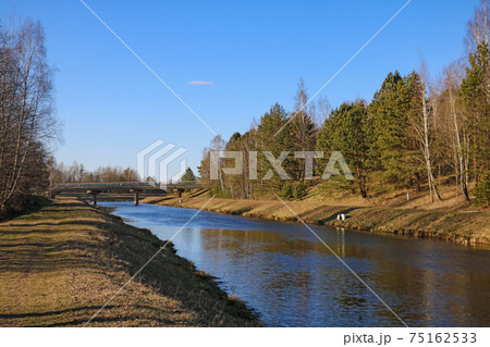 A long river surrounded by trees over a bridge. 75162533