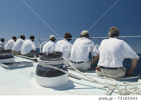 Sailing crew sitting on side of yacht on ocean back view 75165043