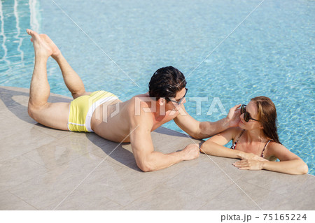 Beautiful young couple man and sexy women wear sunglasses relaxing in swimming poolside. 75165224