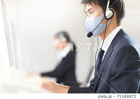 マスクとヘッドセットをつけて働く男性スタッフ マスクとヘッドセットをつけて働く男性スタッフ 75166872