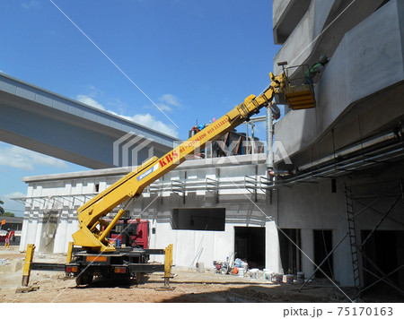 JOHOR, MALAYSIA -MAY 16, 2017: Construction workers standing in the mobile crane bucket while working at high level in the construction site. The bucket movement control by the workers himself. JOHOR, MALAYSIA -MAY 16, 2017: Construction workers standing in the mobile crane bucket while working at high level in the construction site. The bucket movement control by the workers himself. 75170163