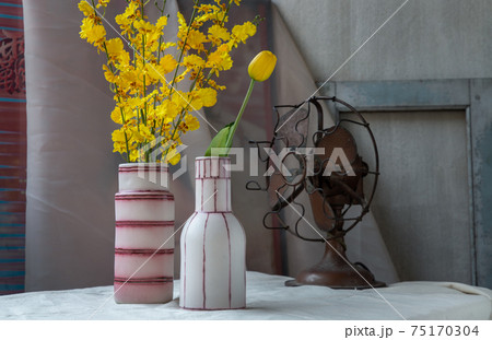 Bouquet of yellow flowers in Two handmade ceramic vase and Vintage fan on white textured table cloth with old cement wall. 75170304