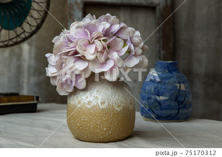 Bouquet of purple flowers in White with yellow handmade ceramic vase and Vintage fan on white textured table cloth with old cement wall. 75170312