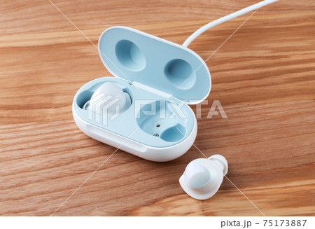 Wireless headphones on a wooden background. Headset close up in the charging case close-up. 75173887