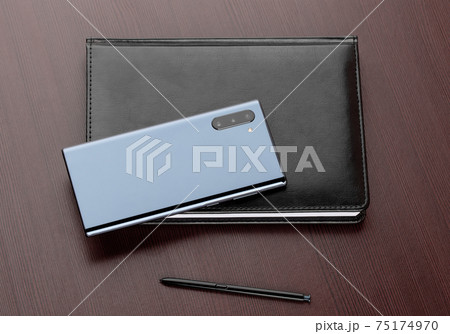 Smartphone with three cameras, notepad, stylus on a wooden table close-up. 75174970