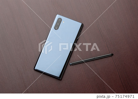 Smartphone with three cameras and a stylus on a wooden table close-up. 75174971