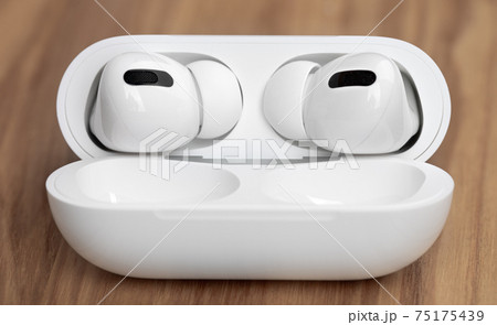 Wireless headphones on a wooden table. Wireless headset and charging case close-up. Wireless headphones on a wooden table. Wireless headset and charging case close-up. 75175439