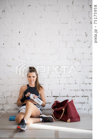 Female fighter exhausted after exercise feeling dehydration, drinks isotonic drink from bottle. Young woman rest after intense training in a boxing studio. 75175958