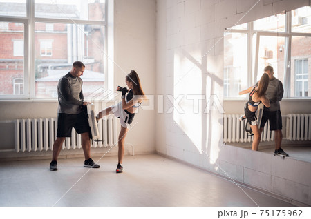 A young female athlete in good physical shape conducts kickboxing training under the supervision of an experienced male coach 75175962