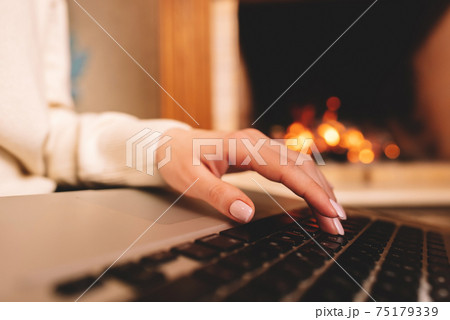 Business woman working on laptop, sitting near cozy fireplace at home. Focus on hands typing on 75179339