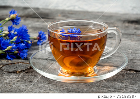 Cup of herbal tea and blue cornflowers flowers on wood background. Cup of herbal tea and blue cornflowers flowers on wood background. 75183587