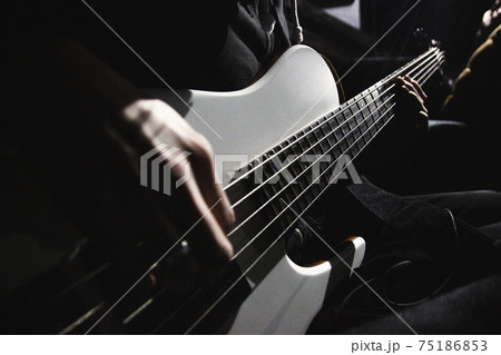 Close up view on five string bass guitar and hands of musician lit by contrast light in dark room 75186853