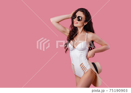 Charming girl in white one-piece swimsuit and straw hat isolated over pink background Charming girl in white one-piece swimsuit and straw hat isolated over pink background 75190903
