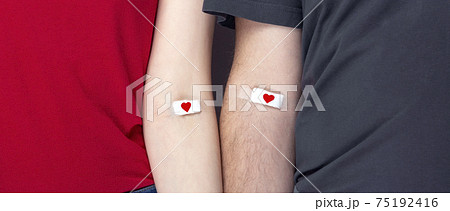 Blood donorship. Man in grey and woman in red T-shirt with hands taped patch after giving blood with red heart 75192416