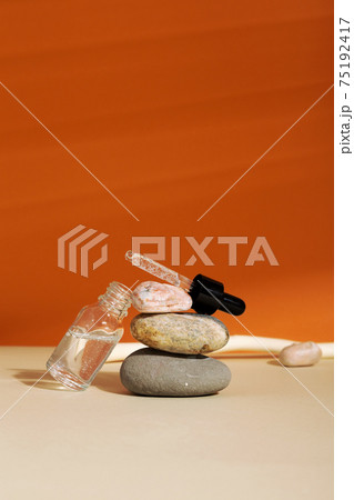 Bottle white glass with dropper on orange background. Natural cosmetic product for skincare concept. Natural materials, rock balancing 75192417