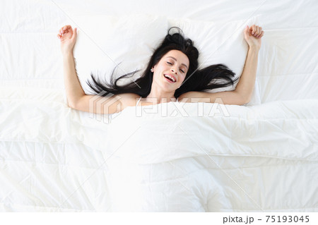 Young woman lying on white bed with closed eyes top view Young woman lying on white bed with closed eyes top view 75193045